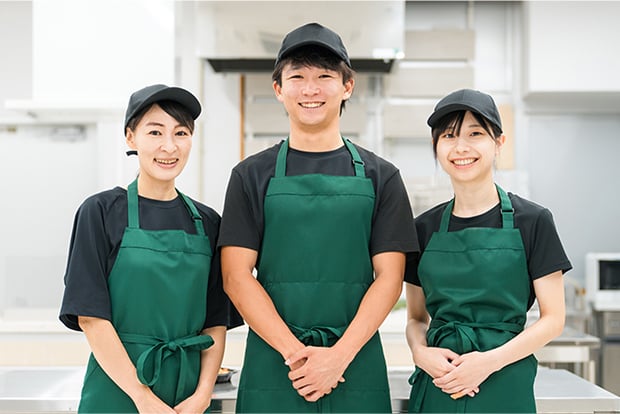 エプロン姿の男性一人と女性二人がこちらを向いて笑顔で立っている写真