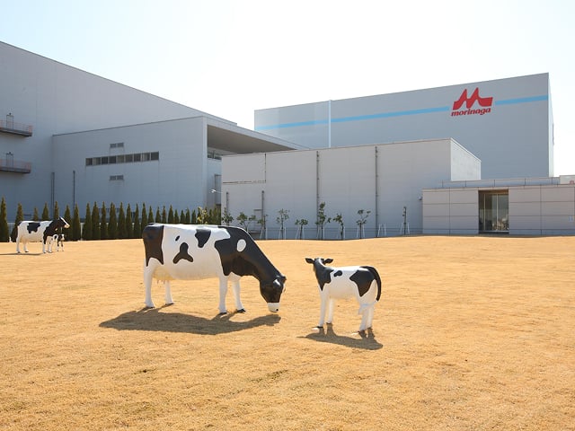 工場を背景に牛3頭の模型が点在している写真
