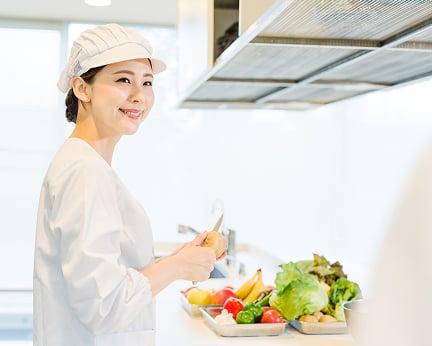 厨房白衣を着た女性が野菜の皮を包丁でむいている様子